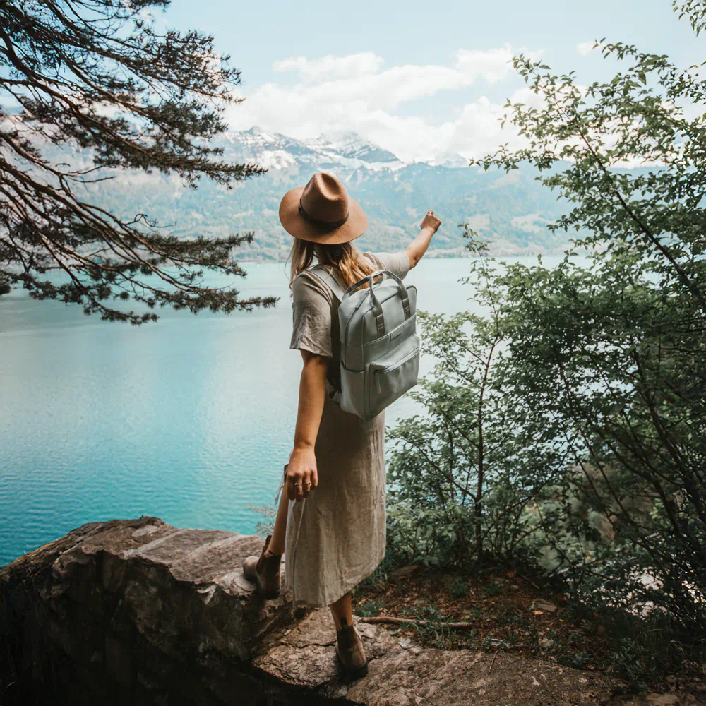 Kobieta w kapeluszu z plecakiem patrzy na jezioro i góry, symbolizując wolność i bezpieczne podróże organizowane przez biuro podróży Travel Well
