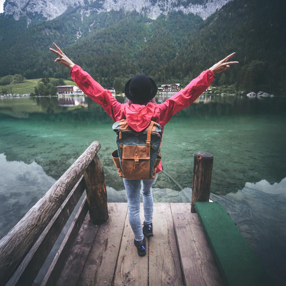 Turysta z plecakiem podnosi ręce w geście radości na tle górskiego jeziora, obrazujący podróże i integracje dla grup zorganizowanych z Travel Well